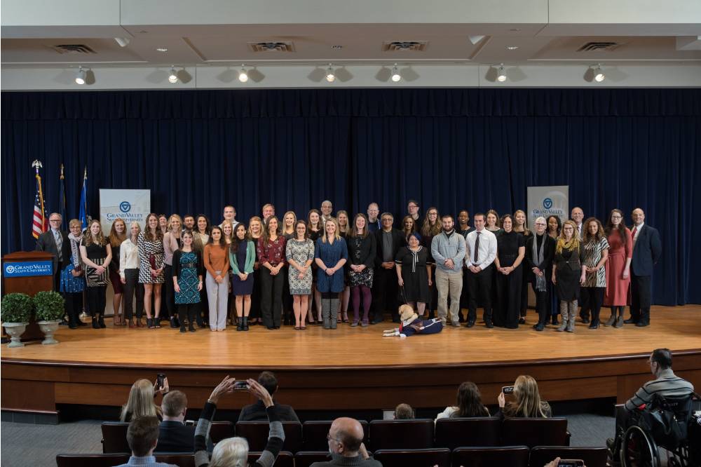 Group photo with all award winners, Mark Luttenton, and Dean Potteiger. People in the first few rows of the audience are visible, some taking photos.